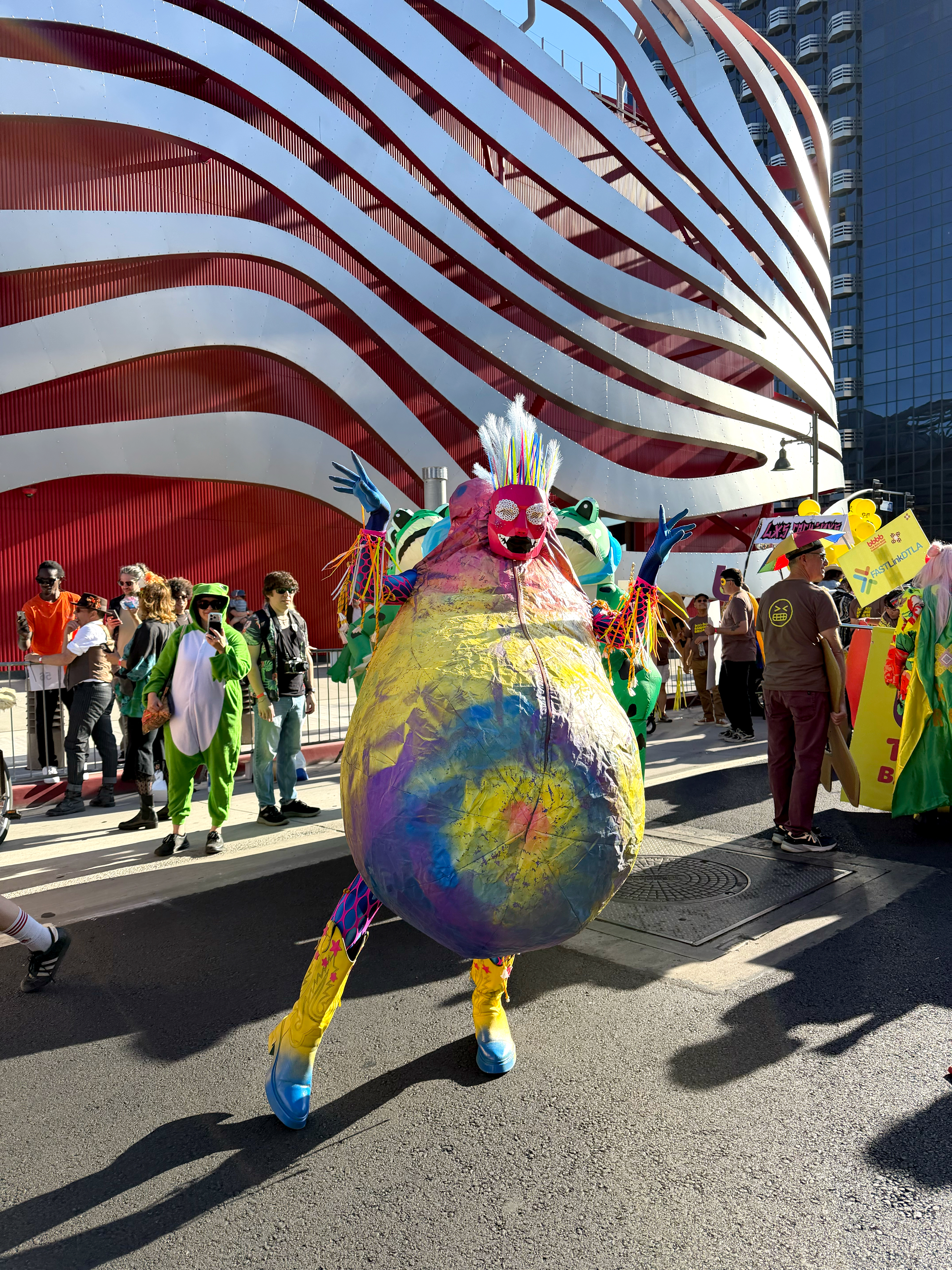 Jesse posing in a Colorful eggplant shaped inflatbale outfit in front of the los angeles automobile musuem.